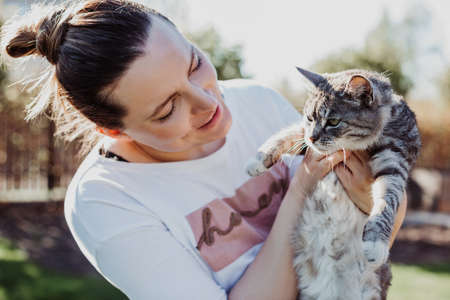 woman admires her pet, holding it in her arms on sunny dayの写真素材