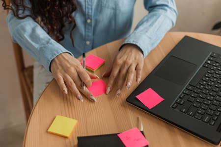 Woman's hands on table near laptop write plans on stickers