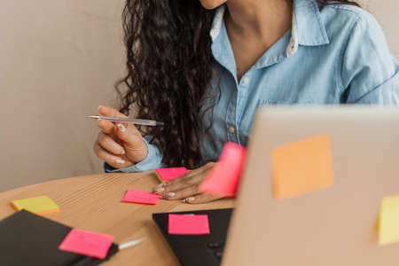 Crop photo of hands of young unrecognizable woman, at working table among computer, stickers and...