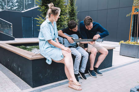 Father and son tuneguitar to play fun song to their mother on summer day in city square. Lifestyle.