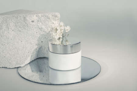 cream box on piece of concrete in cut. Porous structure of concrete is associated with texture of human skin. Composition uses amirror and delicate flower. Medical cosmetics conceptの写真素材
