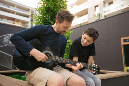 Man teaching teen boy to play guitar in city park on summer dayの写真素材
