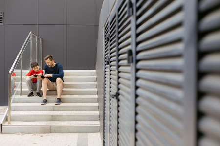 Style of urban life of modern family. Urban view, dad and son are sitting on concrete staircase and spending time togetherの写真素材