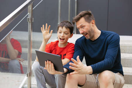 Dad and son make video call using tablet in city on concrete stairs, online communication concept,...