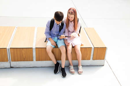 Schoolboy and schoolgirl teenagers get online lesson while sitting in schoolyard, online education conceptの写真素材