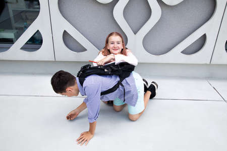 Children teenagers, schoolchildren boy and girl on background of concrete wall. Children laugh and play with school backpacks on backsの写真素材