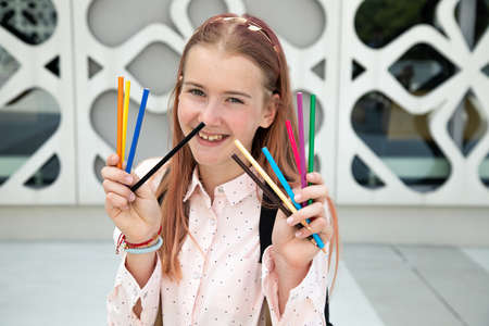 Happy teenage girl with pink hair holding pencils in art space of cityの写真素材