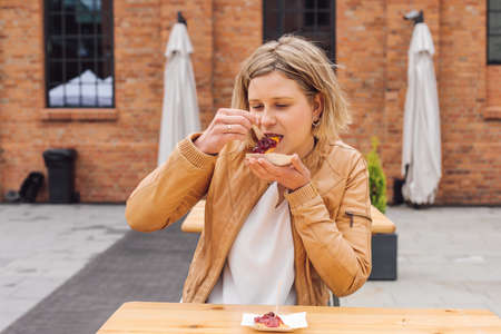 Charming young woman tries fried cheese with lingonberry jam in city street cafe while traveling. Taste and pleasure. Travel and tourism. Lifestyle. It's a great time.Traditional national cuisine.の写真素材