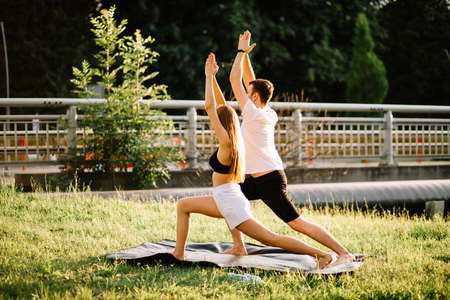 Young couple man and woman doing sports, yoga on city lawn, summer evening, stretching together on sunset, city lifestyleの写真素材