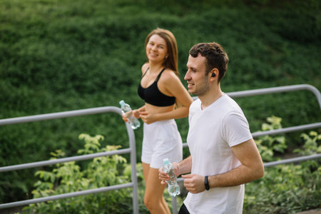 Young happy couple running in city park with botle of water in hands, joint sports, cheerfulness, city sport lifestyleの写真素材