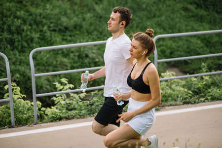 Young happy couple running in city park with botle of water in hands, joint sports, cheerfulness, city sport healthy lifestyle, fitnessの写真素材