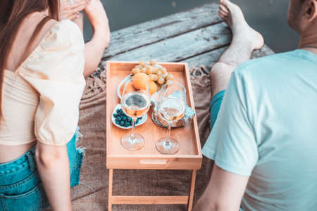 Rear view of young couple on picnic near river or lake, woman and man drinking wine outdoors togetherの写真素材
