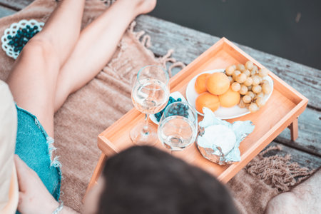 Top view of young happy unrecognizable couple on picnic near river or lake, woman and man drinking wine outdoors together, people having fun on summer vacation, love emotionの写真素材