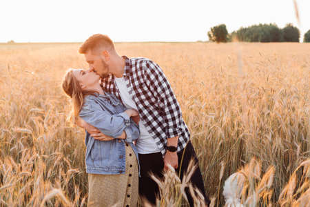 Young pregnant couple is kissing in field during evening walk on summer evening. Pregnancy and care. Happiness and tenderness. Care and attention. Love and hope .Family values.A healthy lifestyle.の写真素材