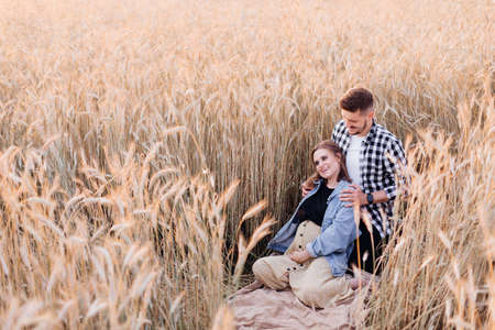 Pregnant young couple enjoys nature on summer evening in field among cereal plants. Family and pregnancy. Love and tenderness. Happiness and serenity. Taking care of new life. Leisure activity.の写真素材
