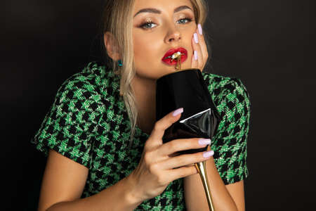 Beautiful young woman with red lipstick on her lips holds glass of wine and jewelry goldfish.の写真素材