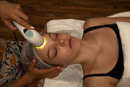 Young woman receiving facial treatment with electroporation beauty device, laser cosmetic, anti acne care, anti aging procedures in spa salonの写真素材