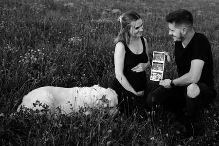 Happy pregnant couple are happy with ultrasound photo of unborn child. Black and white photo. Waiting for child. Pregnancy management. Modern methods of examination.Happy moments of pregnancy.の写真素材