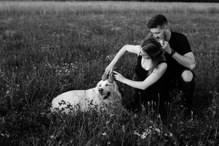 Black and white photo of young pregnant couple who is indulging in walk with their dog, putting children's shoes on her head. Carefree and happy. Waiting for child. Pregnancy. Happy moments.の写真素材