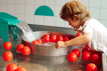 Great opportunity to play with water and bright red balls for boy in children's entertainment center. Tactile sensations. Educational classes and games. Children's entertainment and fun.の写真素材