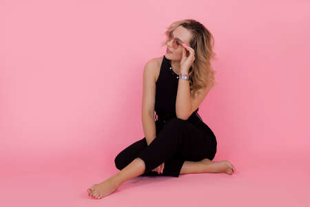 Positive young woman in stylish glasses looking to side while sitting on pink background. High quality photoの写真素材