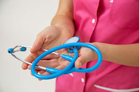 Female doctor in pink medical uniform holds stethoscope in her hands. Life and health insurance. Professional examinations. Medicine and health. Healthy lifestyle. Modern medicine. Medical care.の写真素材