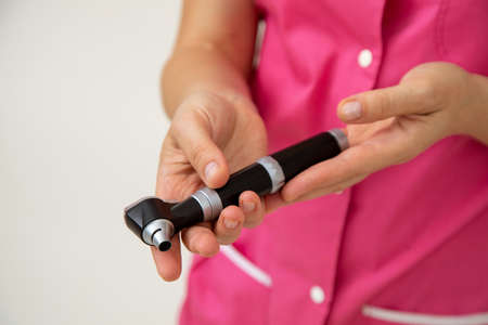 Doctor in pink medical clothes holds otoscope in his hands. Medical research. Preventive examinations. Medicine and insurance. Health protection. Modern medical instruments.の写真素材
