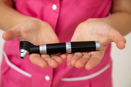 Female doctor in pink medical clothes holds otoscope in her hands. Medical research. Preventive examinations. Medicine and insurance. Health protection. Otoscope.の写真素材