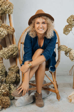 beautiful self-sufficient blonde woman in hat amidst natural decoration of dried hydrangea flowers...