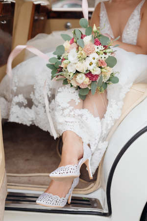 Bride feet in wedding shoes in open car door. Concept of wedding details, celebration, unrecognizable people. High quality photoの写真素材