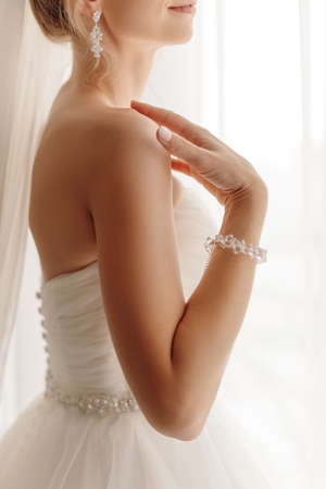 Unrecognizable woman bride standing and looking out window. Wedding bijouterie, earrings and bracelet. High quality photoの写真素材