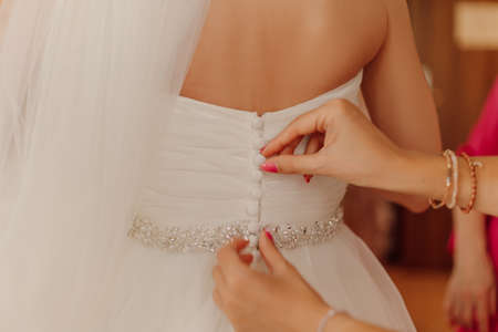 Unbuttoned hands bridesmaids fasten wedding dress. Concept of bride gathering for important day in...