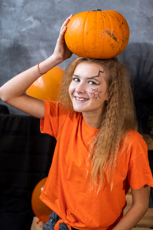 teenage girl among decor for Halloween holiday, huge pumpkin on her head. Close up photoの写真素材