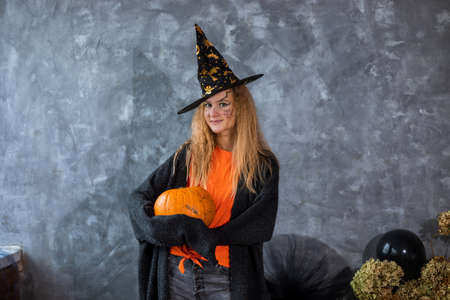 Teenage girl in hat among decor for Halloween holiday, huge pumpkin in her hand. Close up photoの写真素材