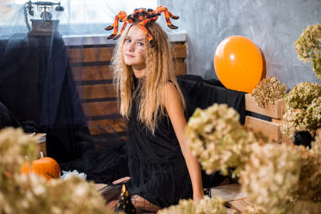 Teenage girl among decor dry flowers for Halloween holiday, huge spider on her head. Close up photo, orange and black colorsの写真素材