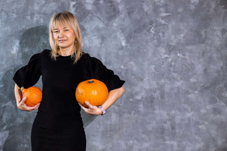 Slender blonde woman in black short dress and heels with pumpkins among Halloween decor, copy spaceの写真素材