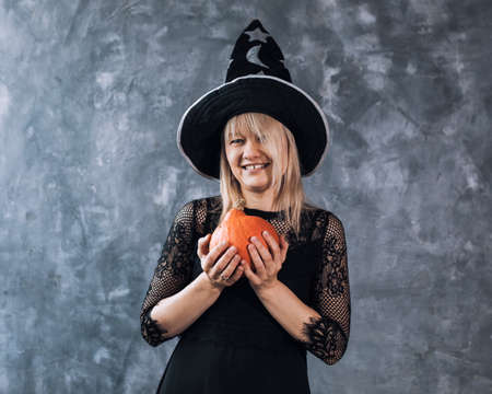 Slender blonde woman in hat and black short dress and heels with pumpkins among Halloween decorの写真素材