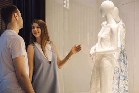 Couple is looking at window of women's clothing store, in which there are mannequins. Recreation and tourism. Shopping malls. Human relations. Shopping. Retail trade. Modern fashion. Consumerism.の写真素材