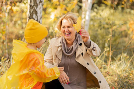 Photo of young woman mom is walking in autumn park with daughter little girl, playing together and...