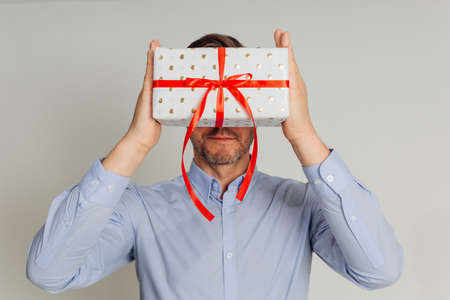 Photo of Unrecognizable man hid behind gift box with red ribbon, holds box in hands in front of face. concept of Valentines Day, international Womens Day, Mothers Day.の写真素材