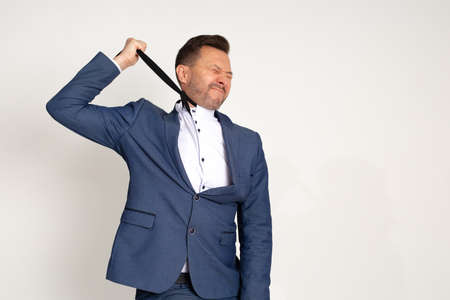 Photo of handsome unemployment business man in expensive suit strangles himself with tie, expression of anguish on face. Chronic fatigue. Debts. Tax debts. Betrayal of partners, midlife crisisの写真素材