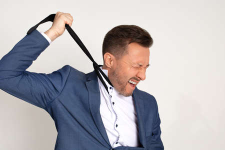 Photo of young handsome business man in expensive suit strangles himself with tie, expression of anguish on face. Chronic fatigue. Debts. Tax debts. Betrayal of partners, midlife crisisの写真素材