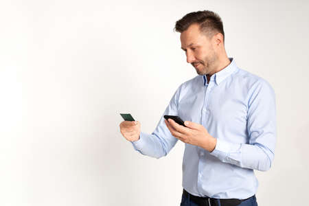 man with smartphone in his hands and credit card on gray background in studio concept of online...