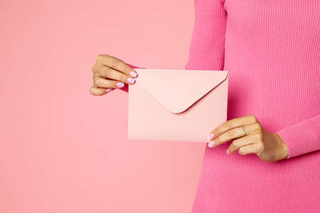 Close-up photo of female handsunrecognizable person holding pink invitation envelope with gift certificate, postcard, wedding invitation card. Consept of birthday present, Valentine's dayの写真素材