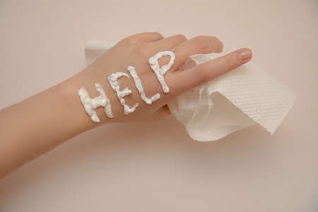 Concept of painful dry skin. Sign help written with cream on woman's hand with delicate manicure....