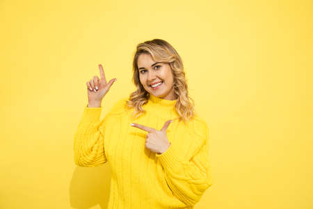 Young cute beautiful blonde surprised woman wearing yellow sweater standing over yellow isolated...