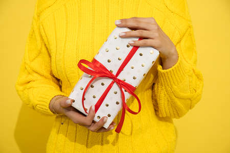 Unrecognizable Woman in sweeater holding in hand present, gift box on yellow background. Close-up photo, Gift Concept.の写真素材