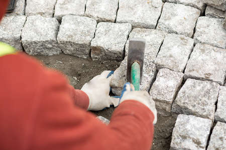 worker made sidewalk from bricks using hammer in hand, over the shoulder view.