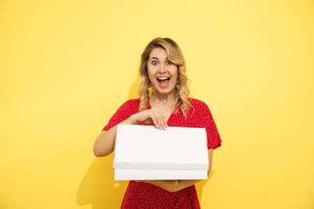 Young, beautiful long-haired blonde woman in red dress, joyfully opens white box with space for an...