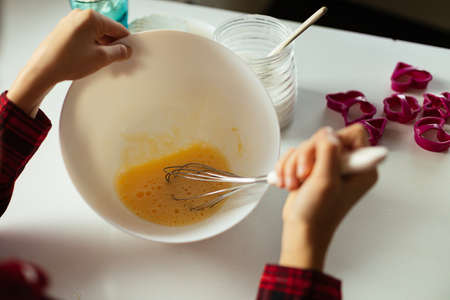 unrecognizable person whips egg in bowl with whisk. view from over shoulder. cooking at home. teenager's hobby, baking conceptsの写真素材